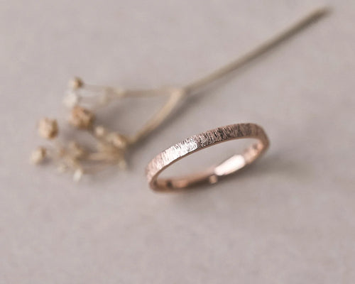 Angled view of 18ct rose gold horn texture wedding ring with dried flowers