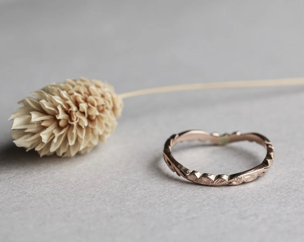 Rose gold ring with textured design on a gray surface with a beige flower.
