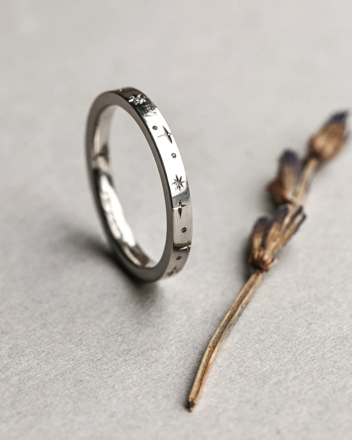 Silver ring with engraved patterns on a gray surface with a dried plant.