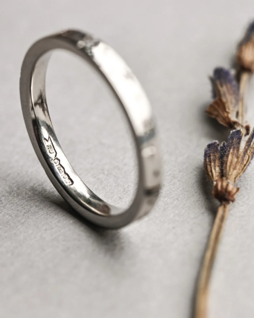 Silver ring on a light gray surface with dried flowers.