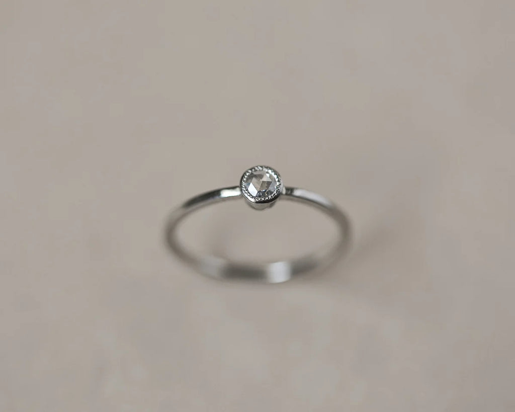Silver ring with a small diamond on a beige background