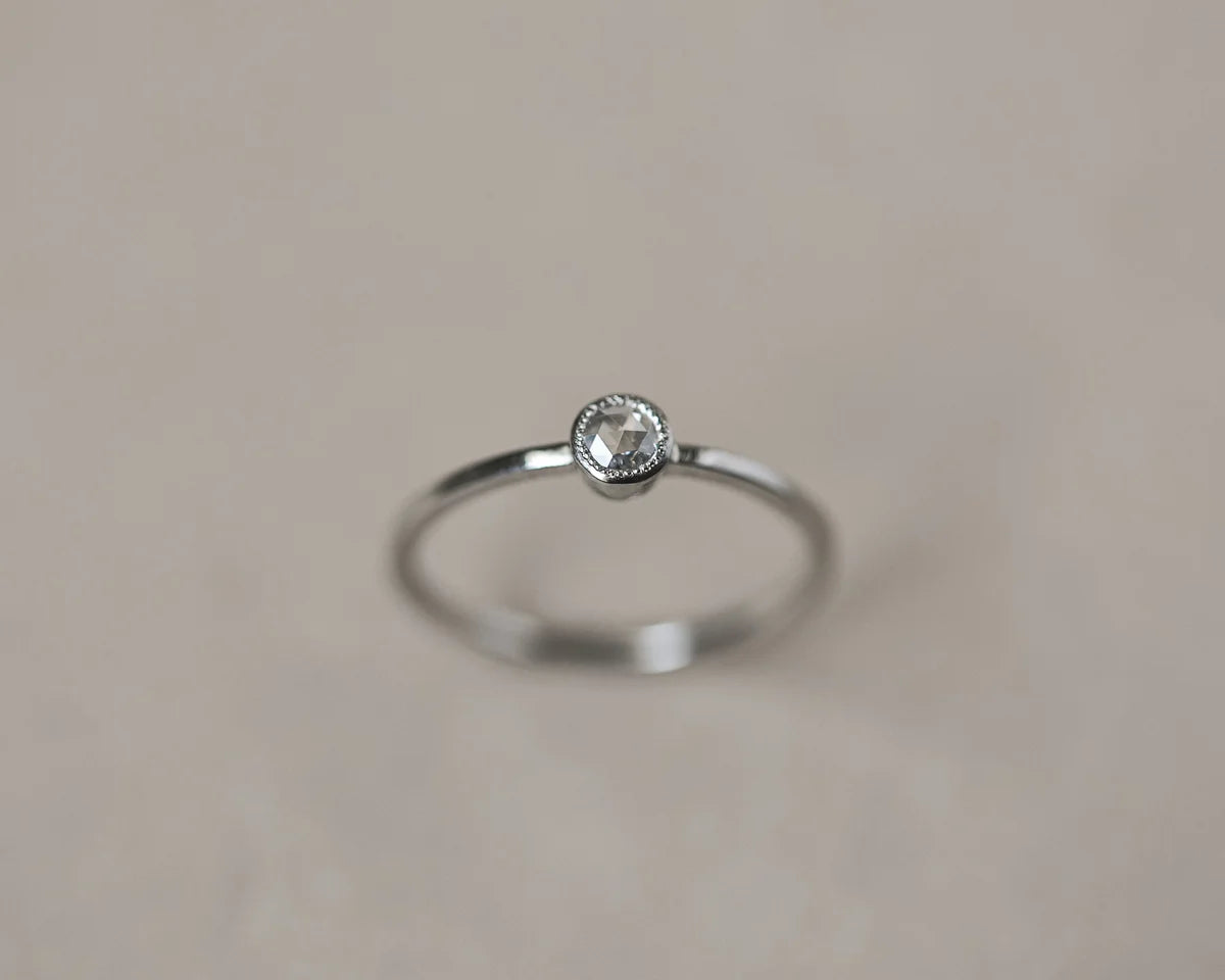 Silver ring with a small diamond on a beige background