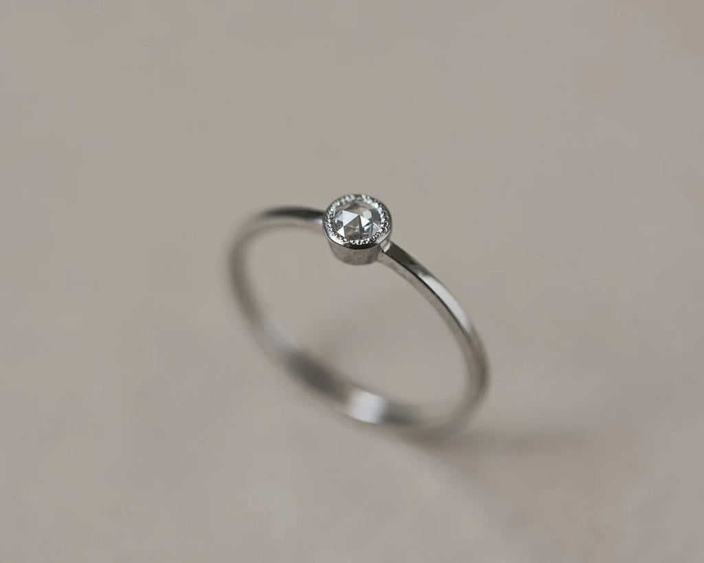 Silver ring with a small diamond on a beige background