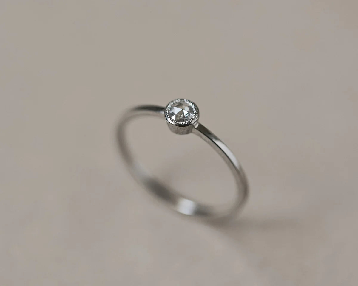 Silver ring with a small diamond on a beige background