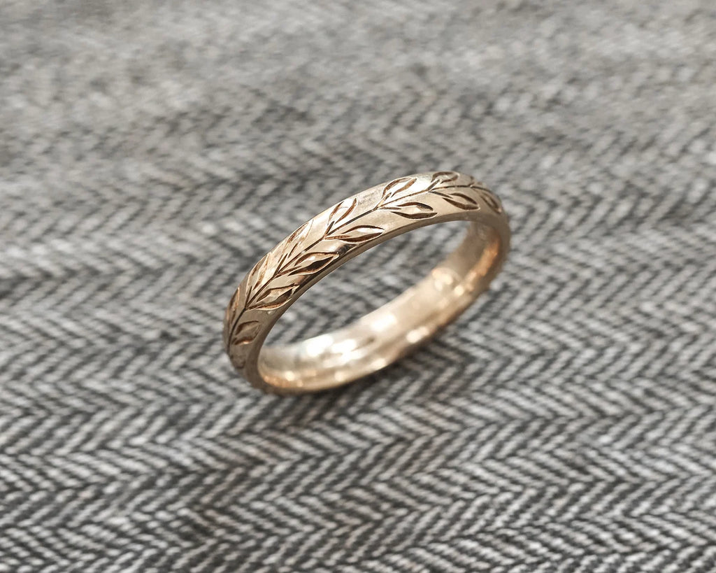 Side view of hand engraved olive leaf wedding ring on fabric