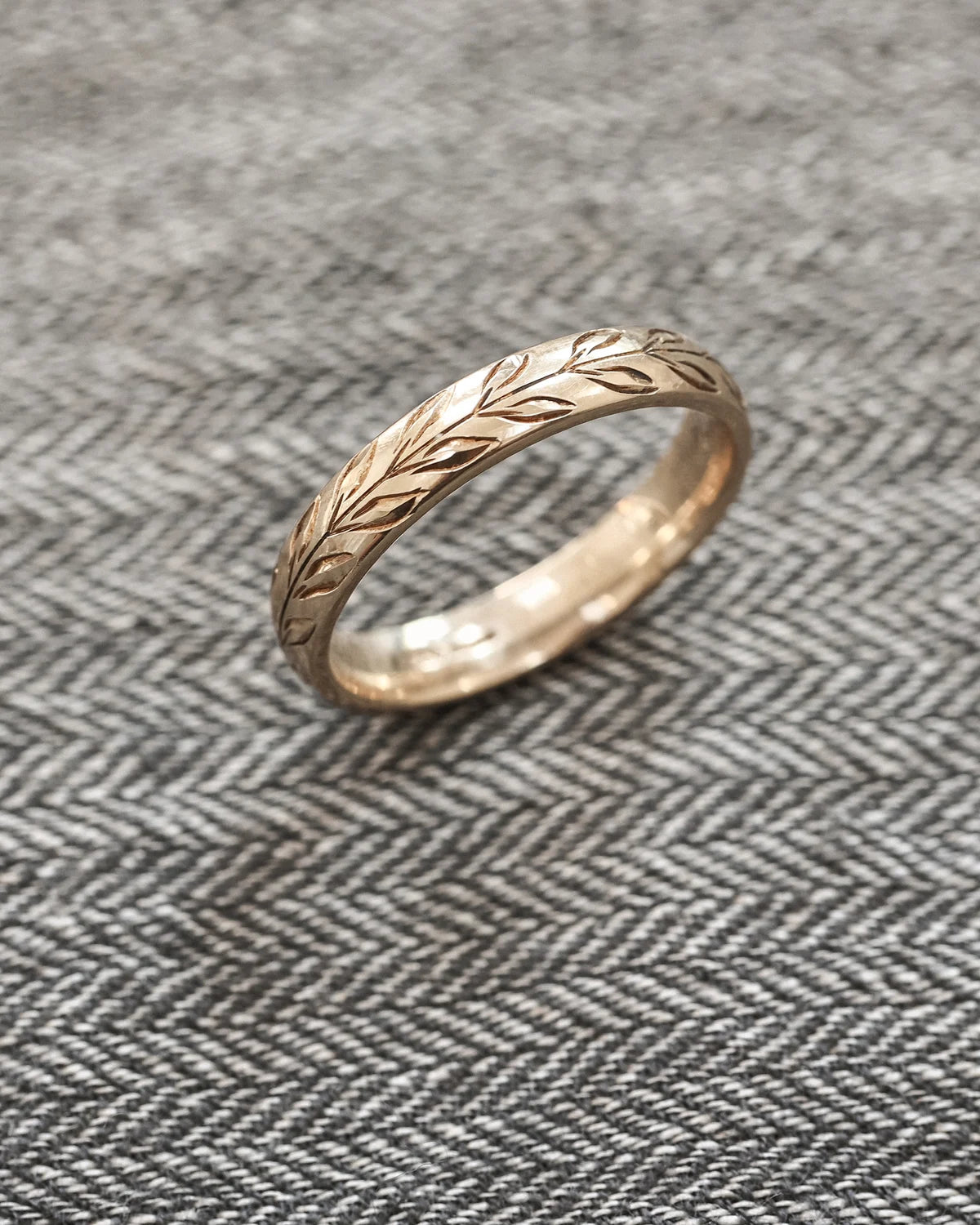 Angled view of 9ct yellow gold olive leaf wedding band on textured fabric