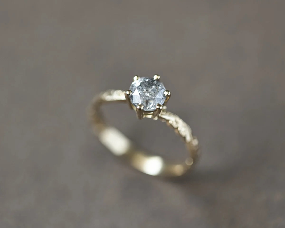 Soft focus view of 18ct yellow gold grey diamond engagement ring