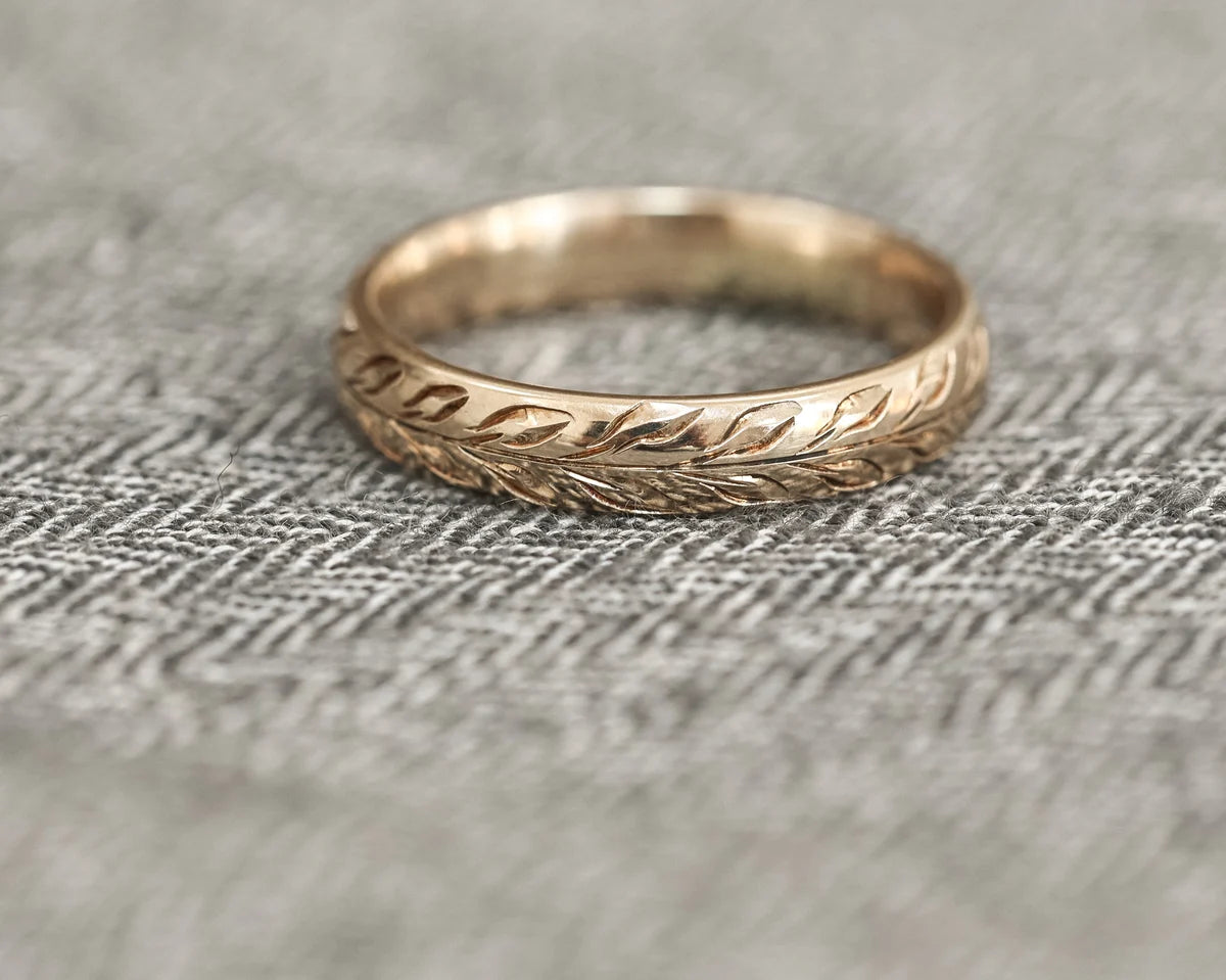 Olive leaf engraved yellow gold wedding ring on herringbone fabric