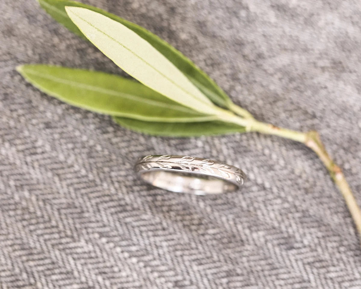 Minimal platinum olive leaf engraved wedding ring on herringbone fabric