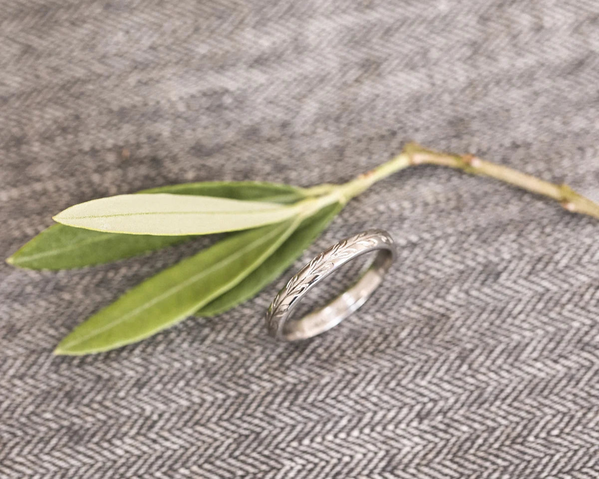 Angled view of 3mm platinum olive leaf wedding band with olive branch
