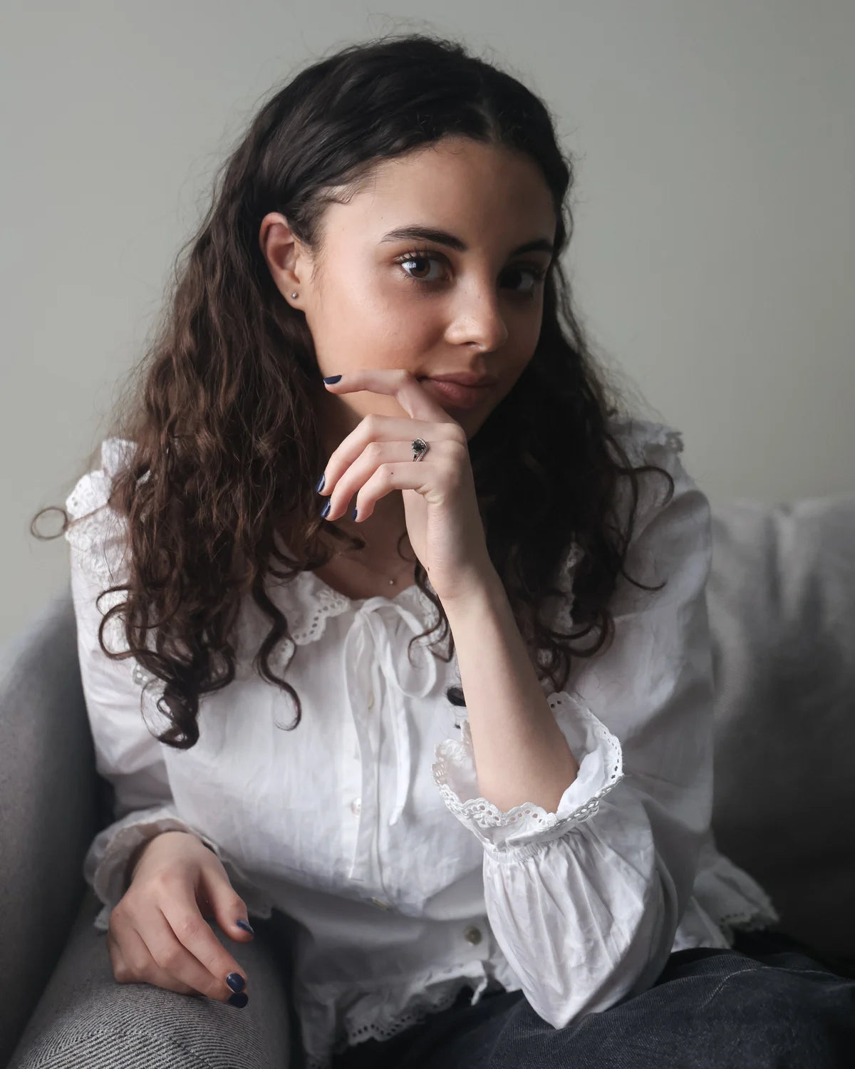 Woman in a white blouse sitting on a couch with a neutral background