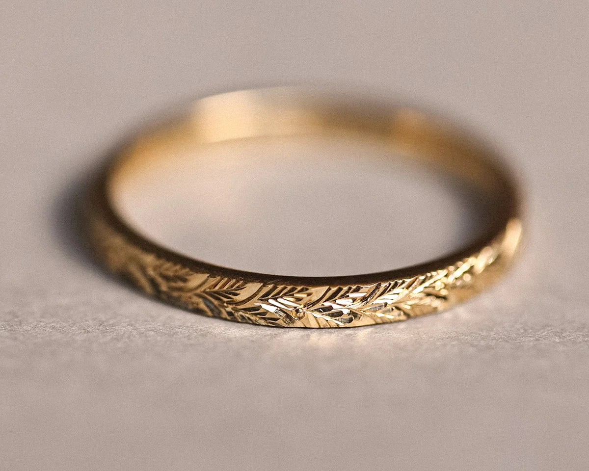 Close-up of hand engraved laurel leaf motif on yellow gold band