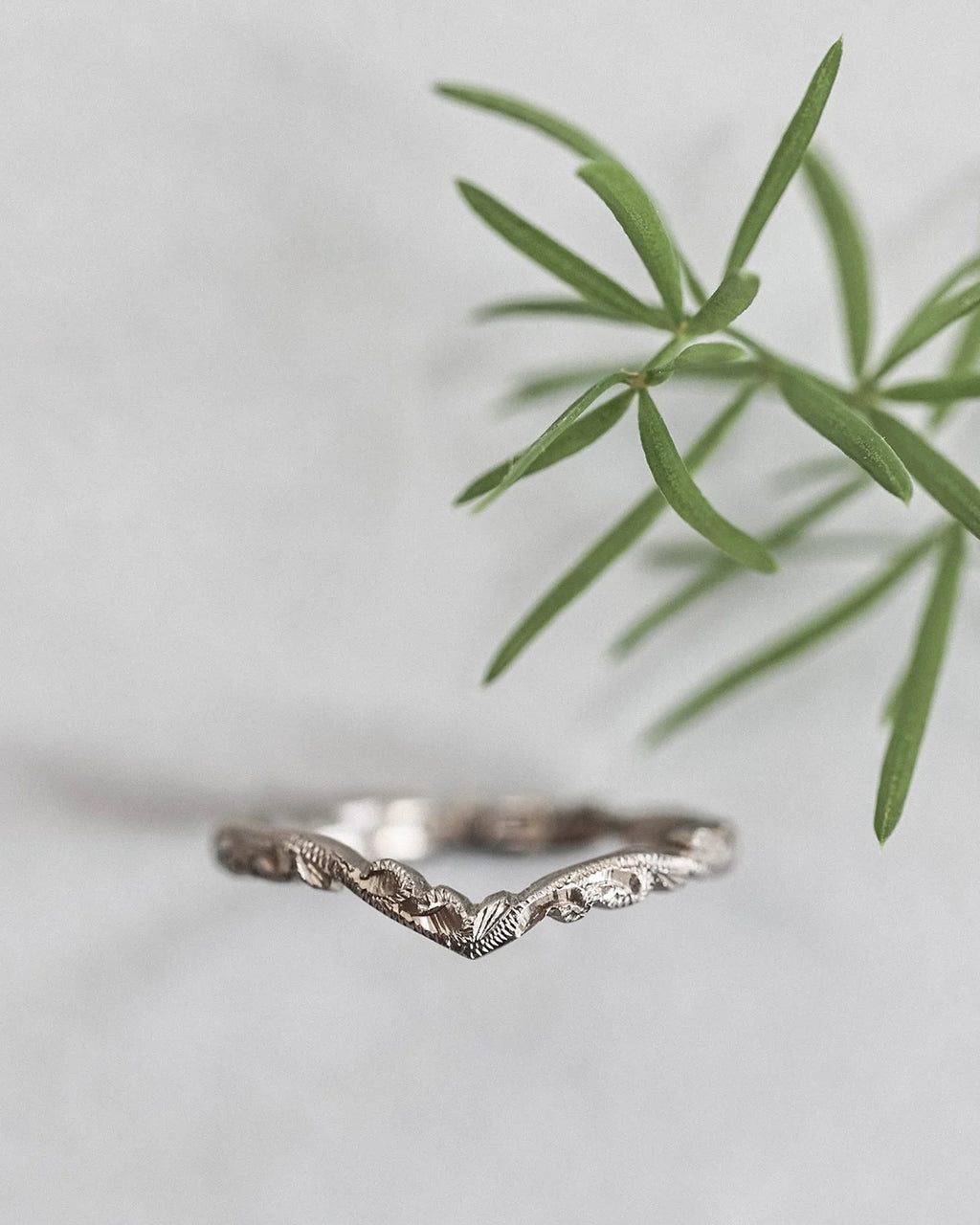 Silver ring with leaf design on a light gray background with green leaves.