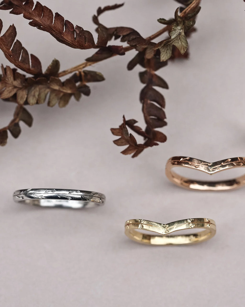 Three rings in silver, gold, and rose gold on a light background with leaves.