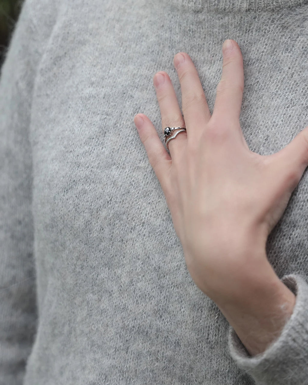 A close-up of a person's hand resting on a light gray knit sweater, wearing a silver ring with a small dark stone.
