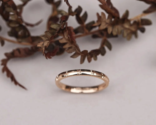 Rose gold ring with engraved details on a white surface with dried leaves.