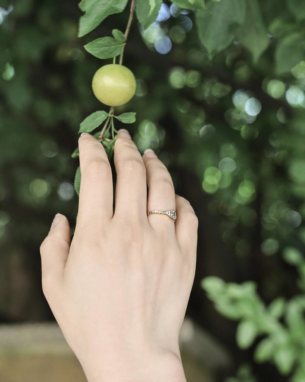 Laurel leaf diamond ring worn on hand with green fruit tree