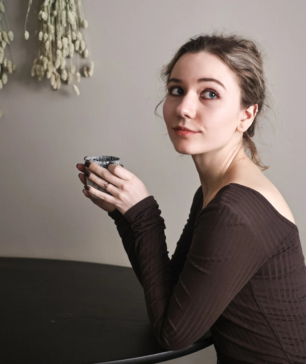 Woman holding a mug against a neutral background wearing gold champagne diamond studs