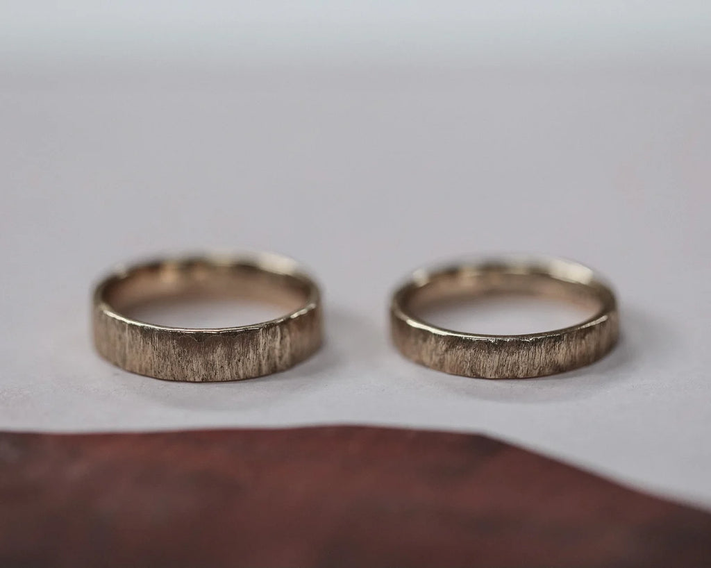 Two gold rings with textured band on a light gray background
