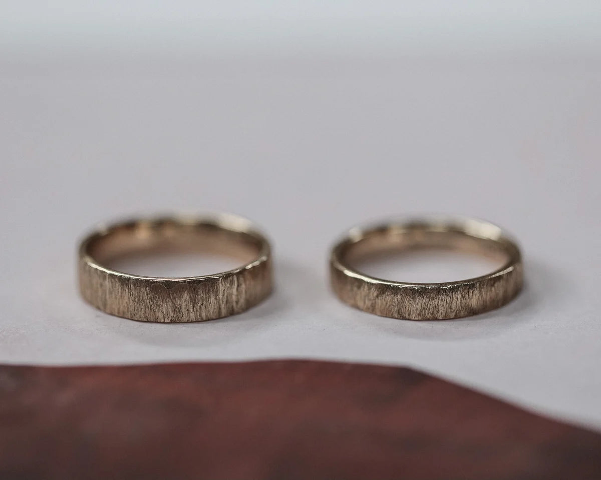 Two gold rings with textured band on a light gray background