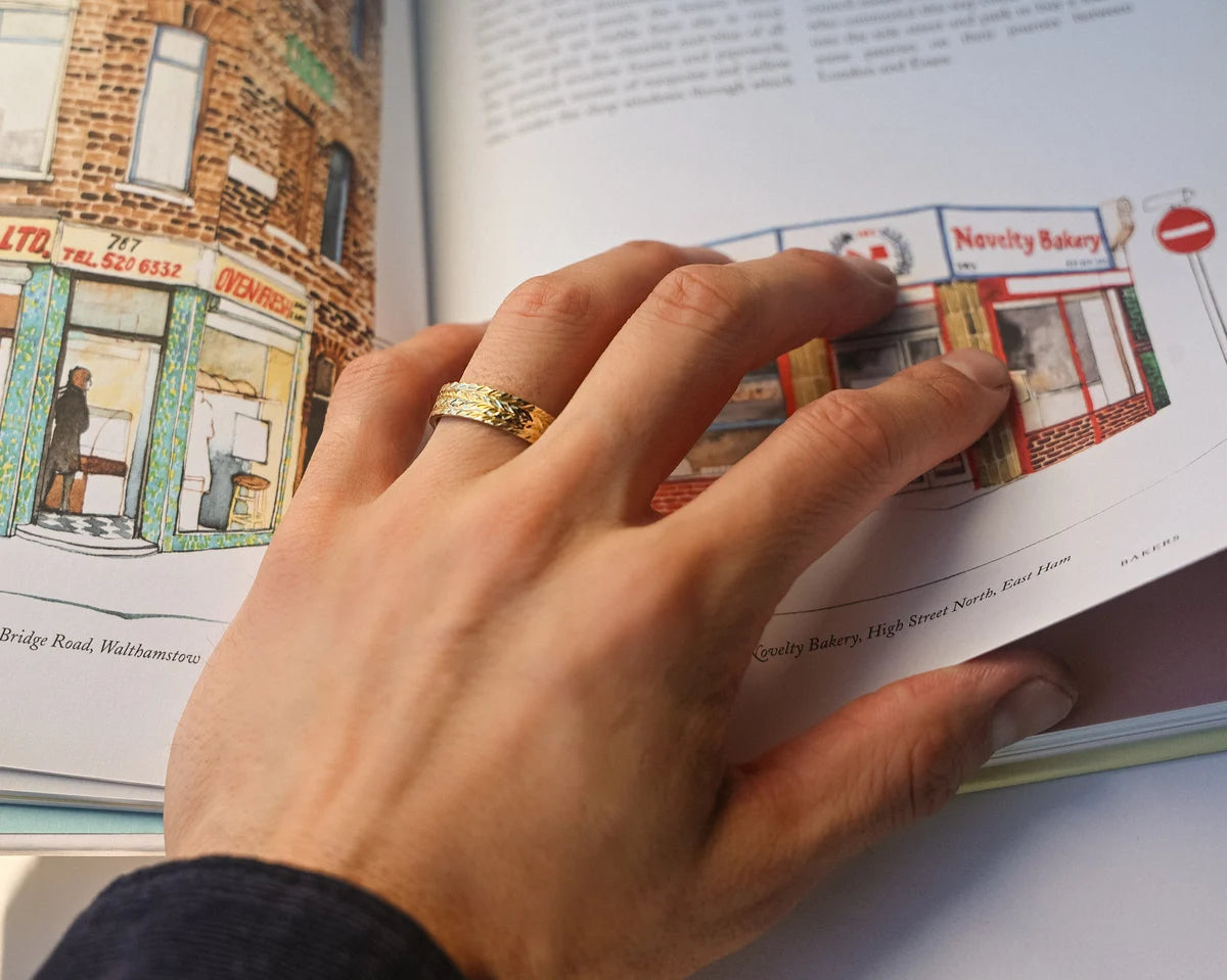 Herringbone engraved yellow gold wedding ring worn while reading illustrated book