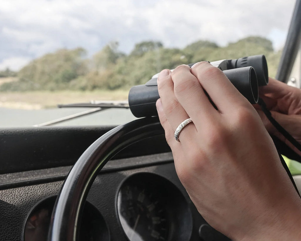 Hand holding binoculars with a scenic view outside a vehicle window.