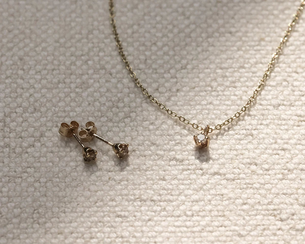 Gold necklace and earrings on a textured beige surface