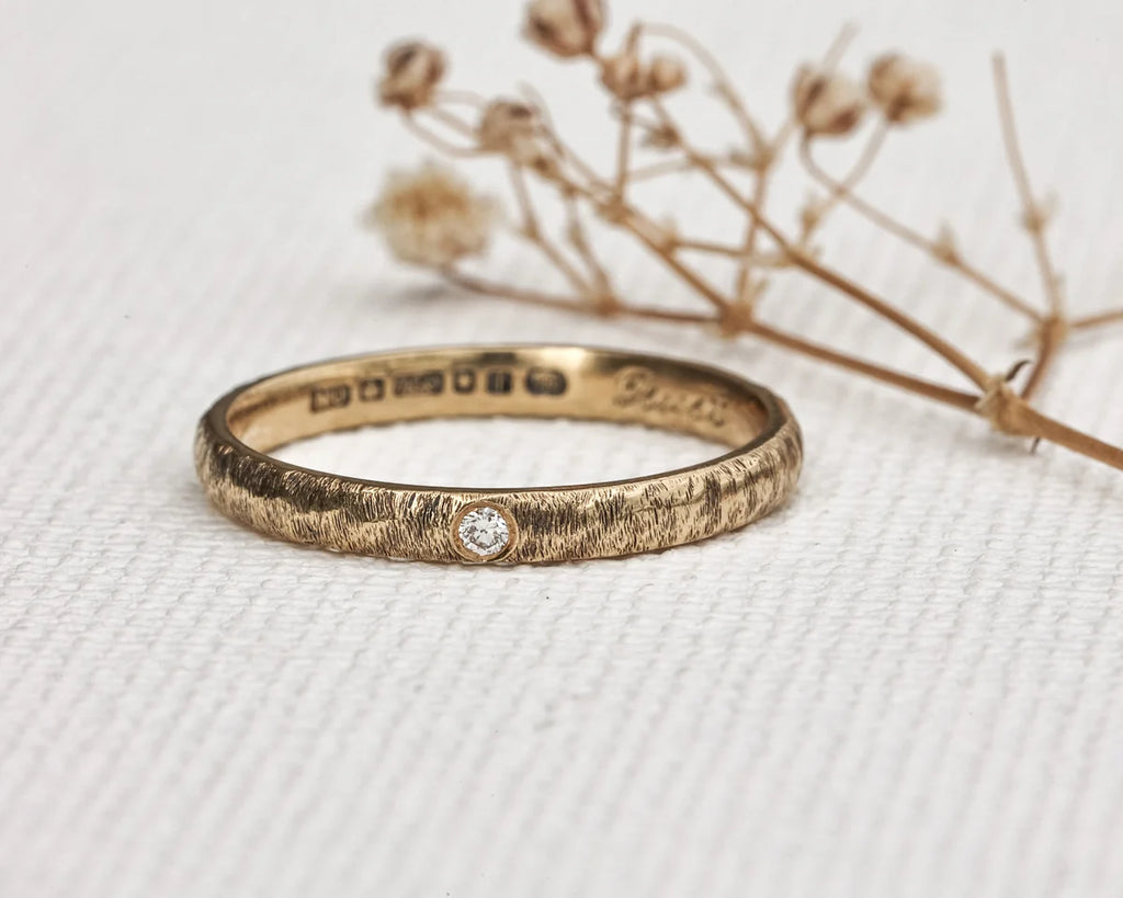 Gold ring with diamond on a textured white surface with dried flowers.