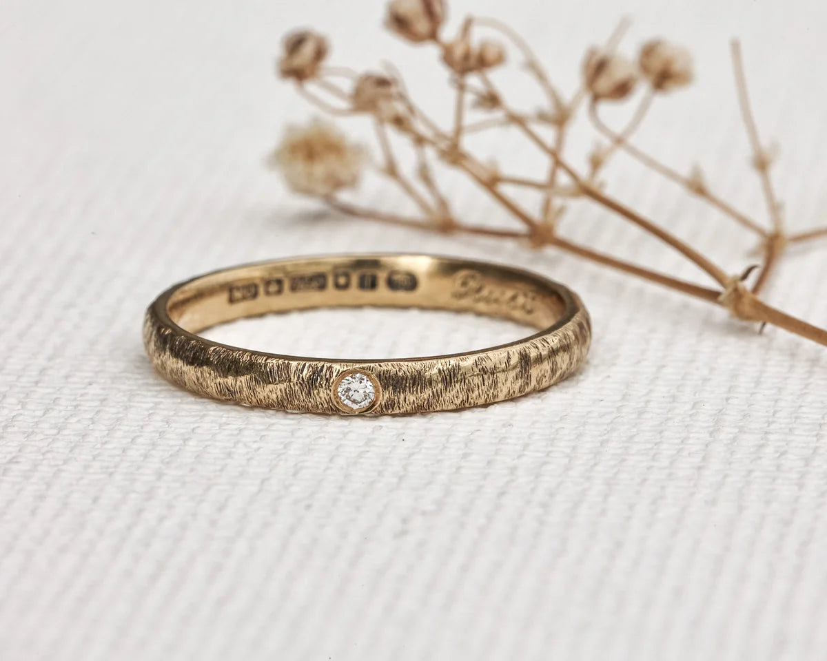 Gold ring with diamond on a textured white surface with dried flowers.