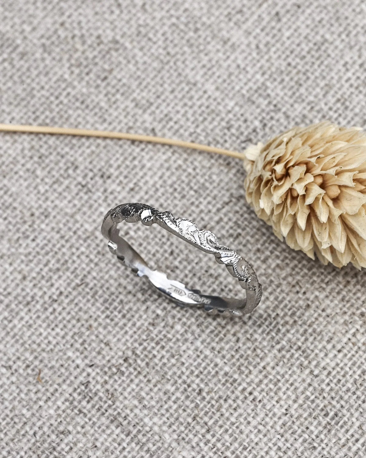 Silver ring with a natural, tree bark texture on a textured gray surface with a dried flower.