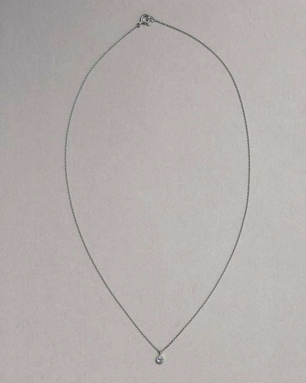 Thin silver necklace with a small pendant on a light gray background