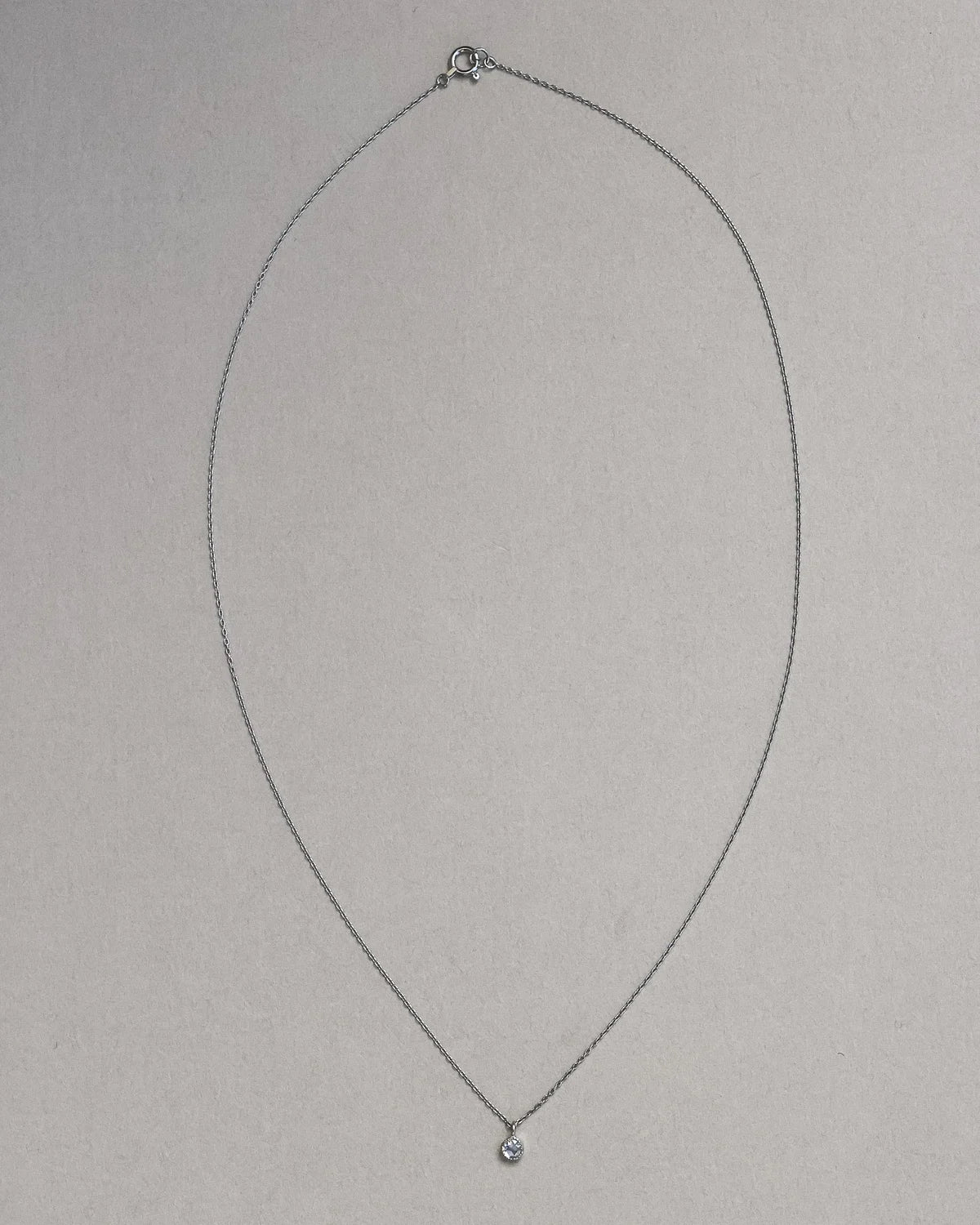 Thin silver necklace with a small pendant on a light gray background