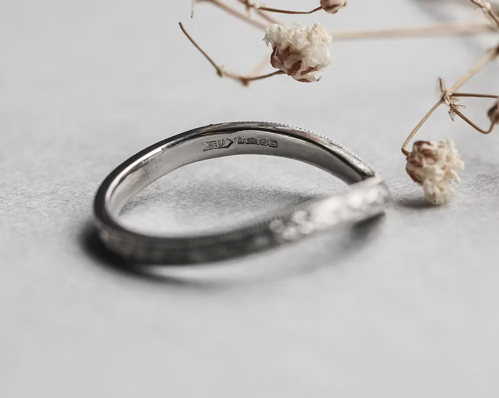 Silver ring with '925' stamp on a light gray surface with dried flowers.