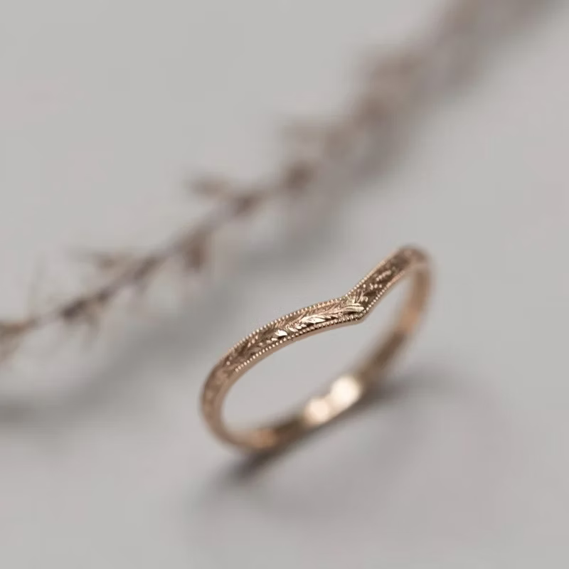 Rose gold ring with intricate design on a soft gray background