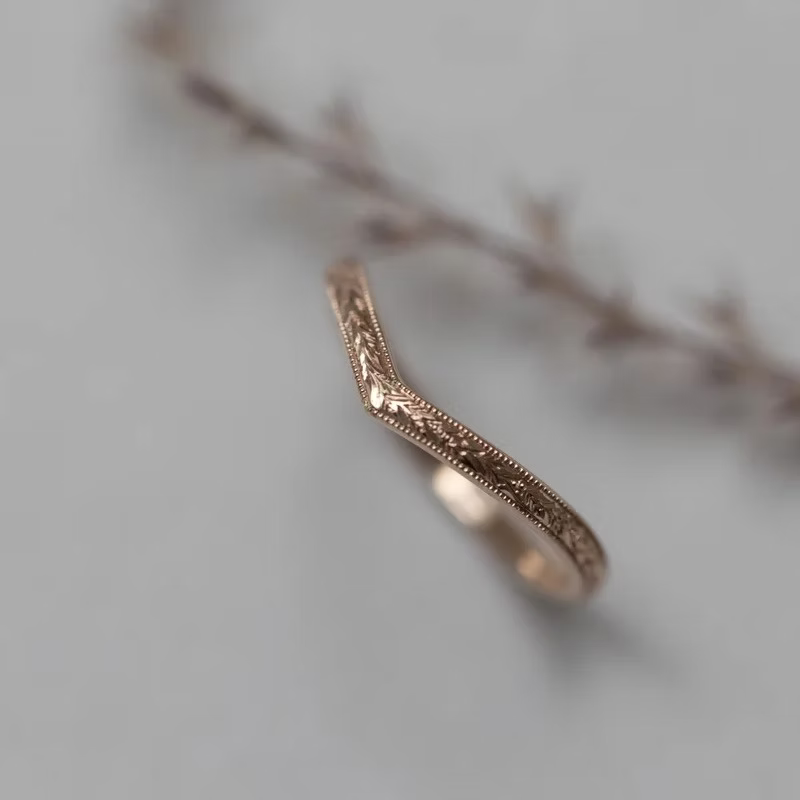 Rose gold ring with intricate design on a soft gray background