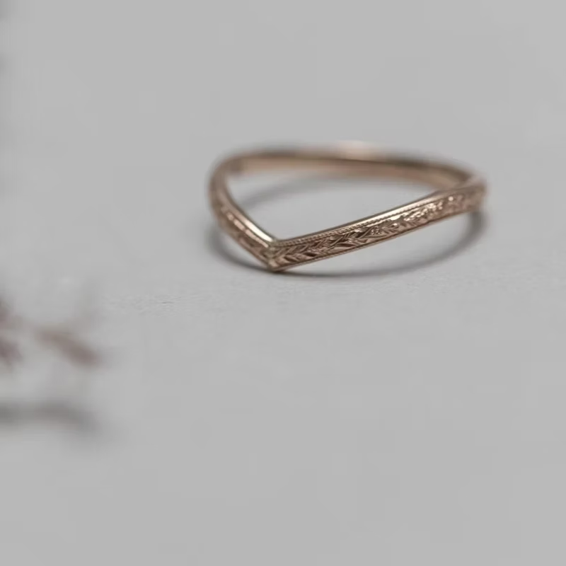 Rose gold ring with intricate design on a light gray background