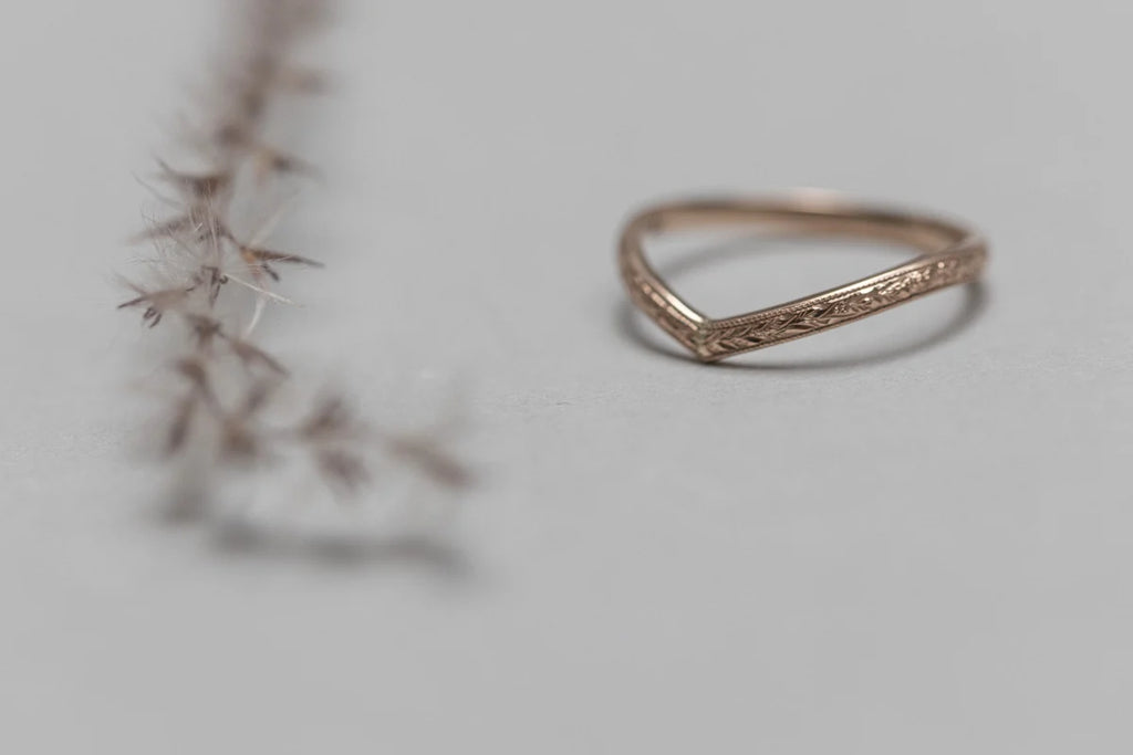 Rose gold ring with intricate design on a light gray background