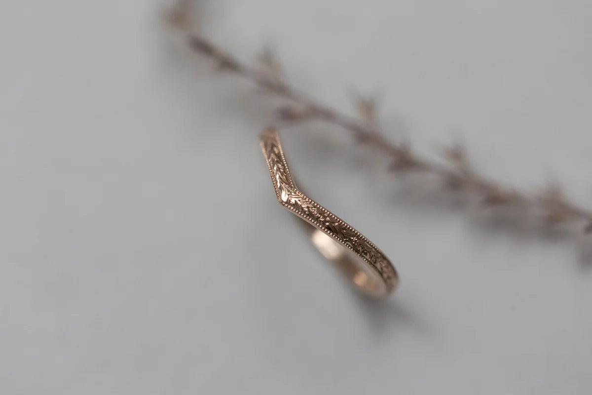 Rose gold ring with intricate design on a light gray background