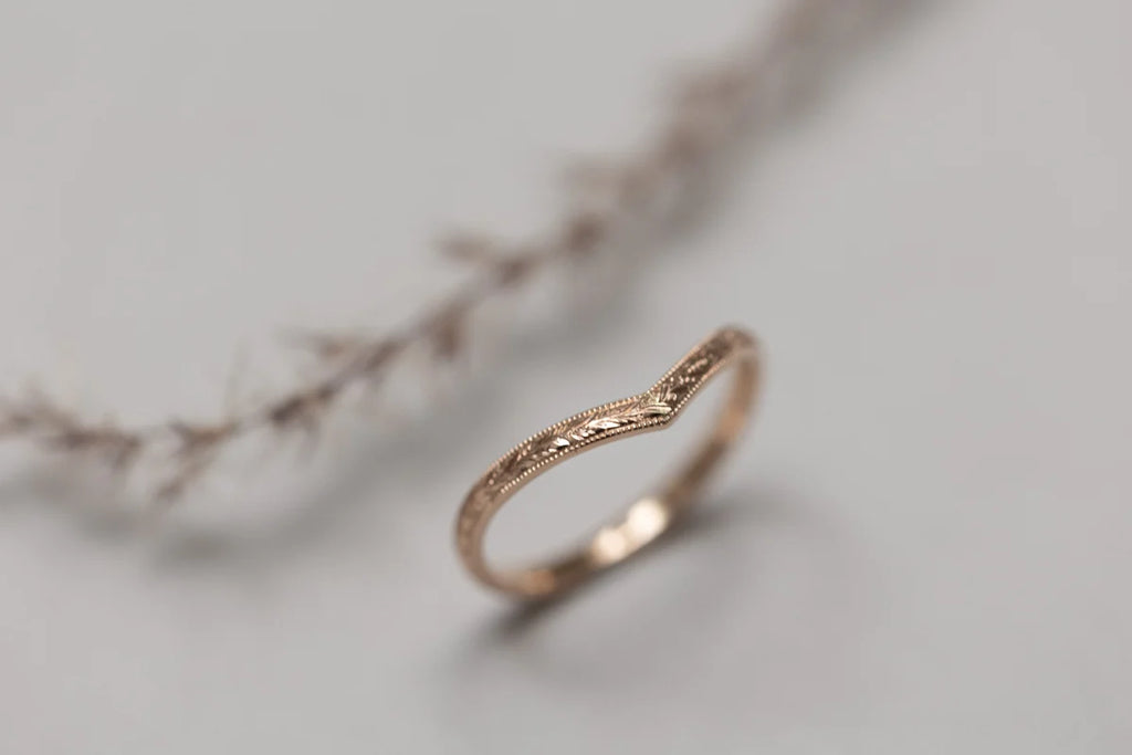 Rose gold ring with intricate design on a light gray background