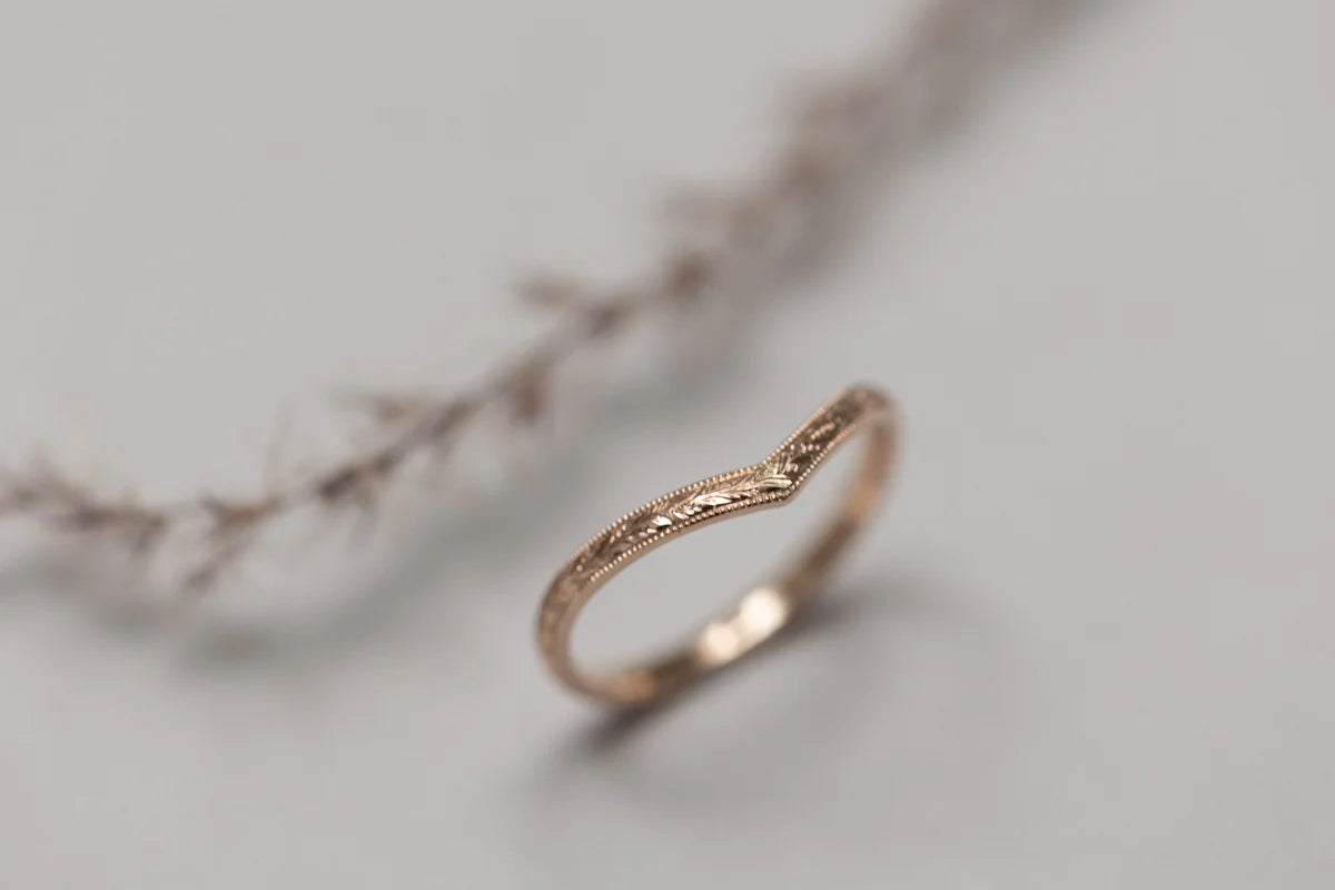 Rose gold ring with intricate design on a light gray background