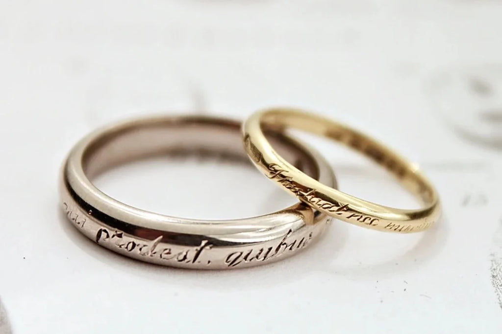 Two gold rings with engraved text on a light background