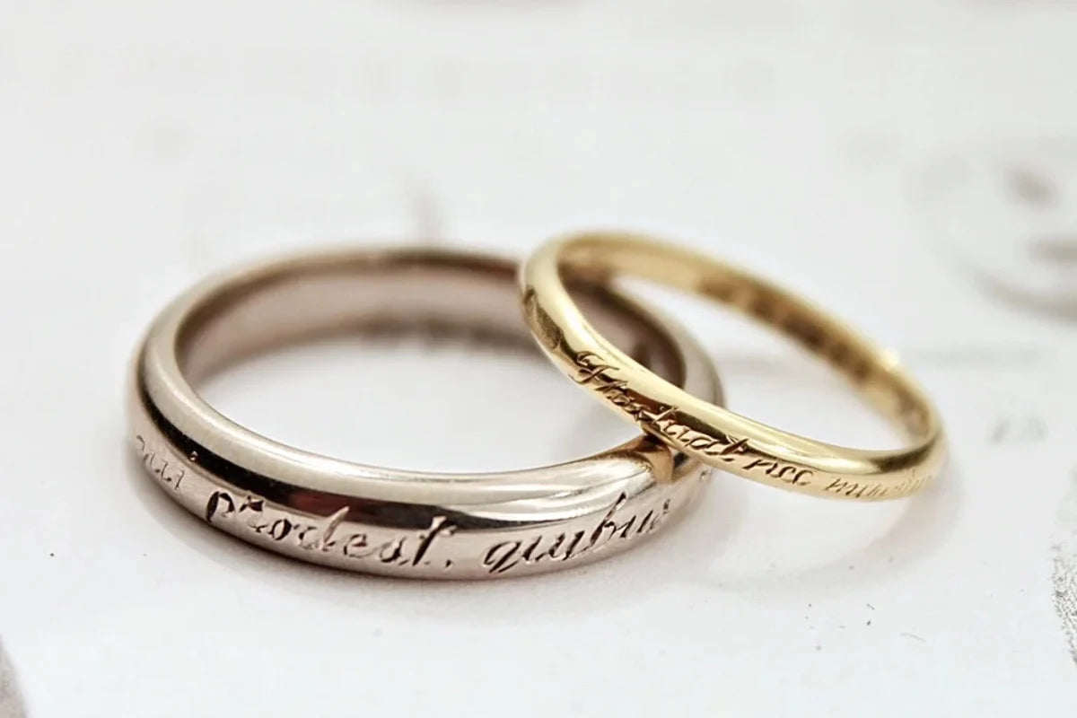 Two gold rings with engraved text on a light background