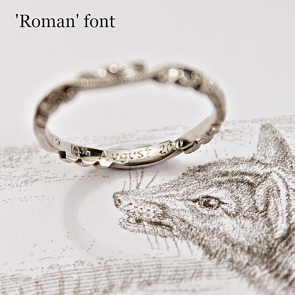 Silver ring with 'August 2023' engraving on a textured surface with a wolf illustration.